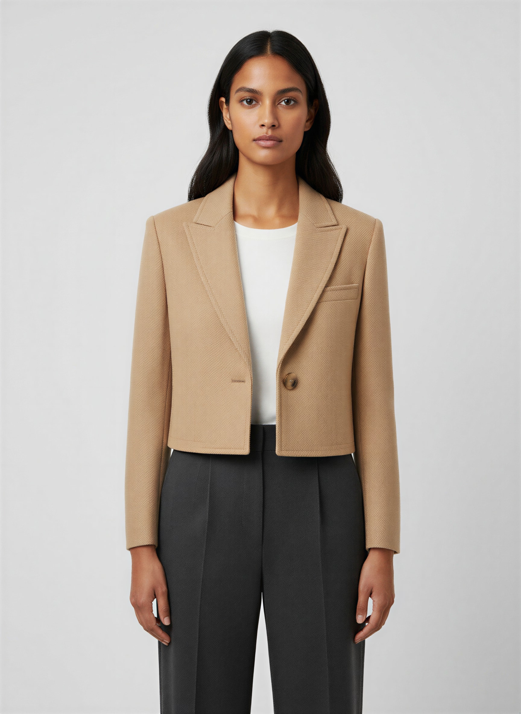 Vrouw in een zandkleurige cropped blazer over een wit shirt, rechtop naar de camera