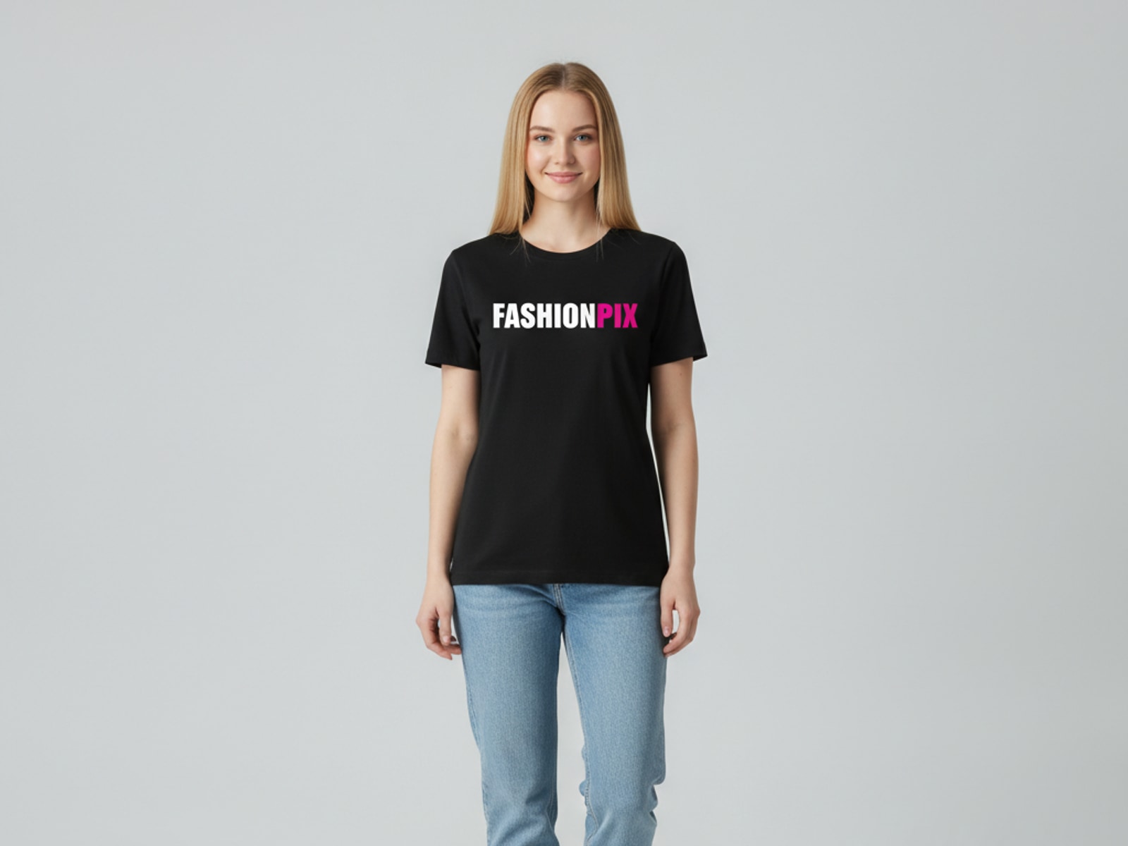 Jong vrouwelijk model met lang blond haar draagt hetzelfde zwarte FASHIONPIX-T-shirt met een lichte jeans, tegen een lichtgrijze studioachtergrond