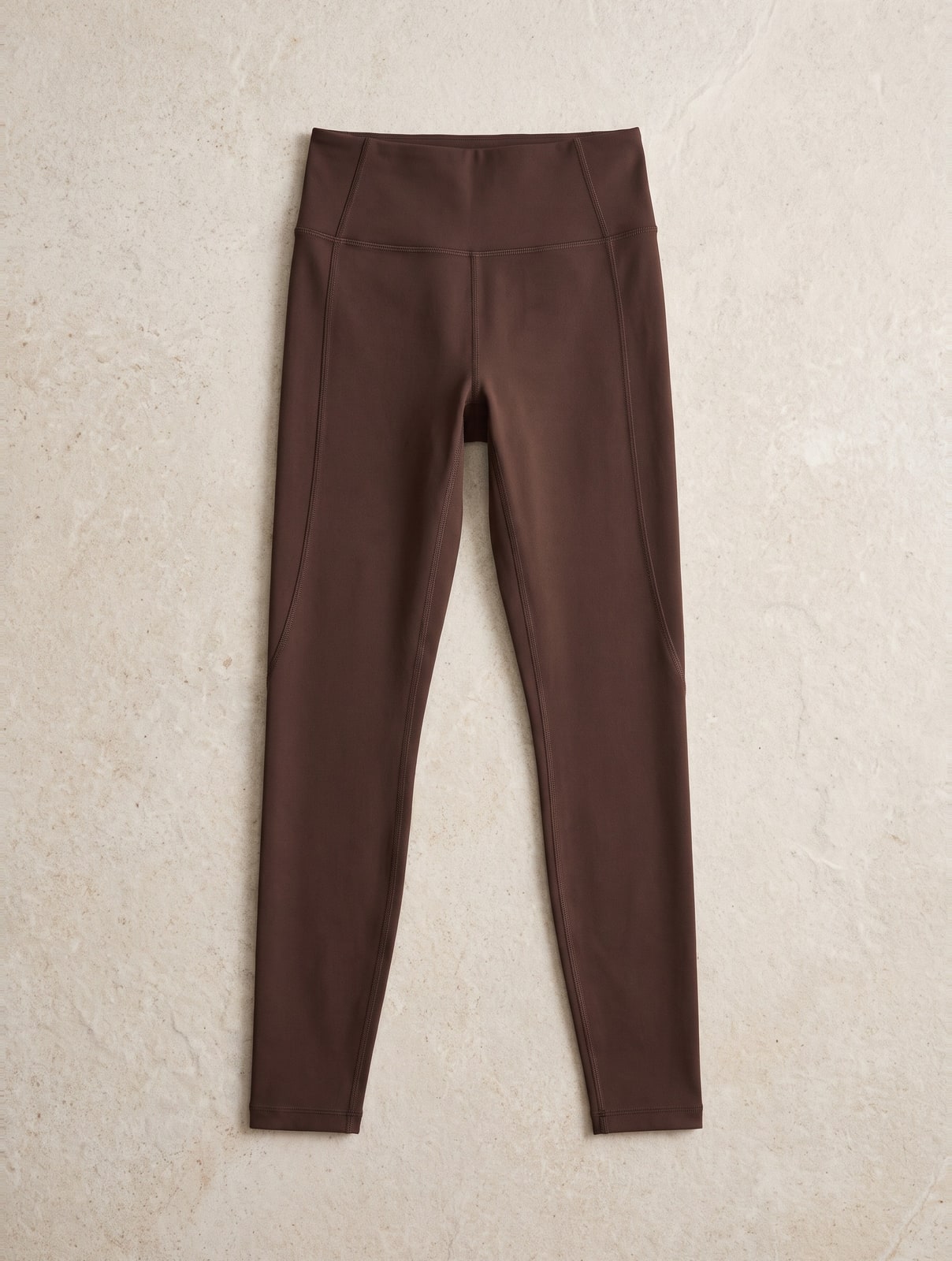 Espressobruine naadloze sportlegging met hoge taille, platgelegd op een lichte stenen ondergrond