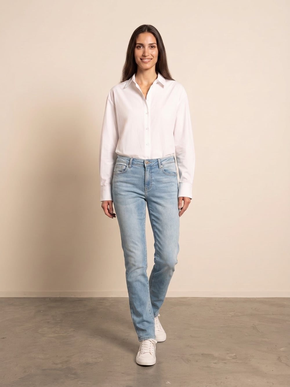 Sara draagt een lichtblauwe jeans met rechte pijp bij een witte blouse, recht van voren, glimlachend