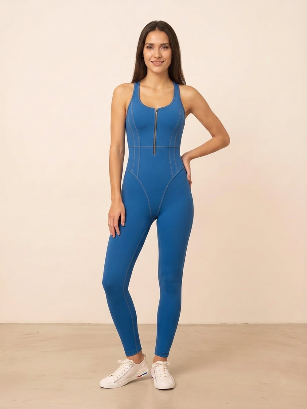 Dezelfde kobaltblauwe jumpsuit, driekwart met de hand in de zij